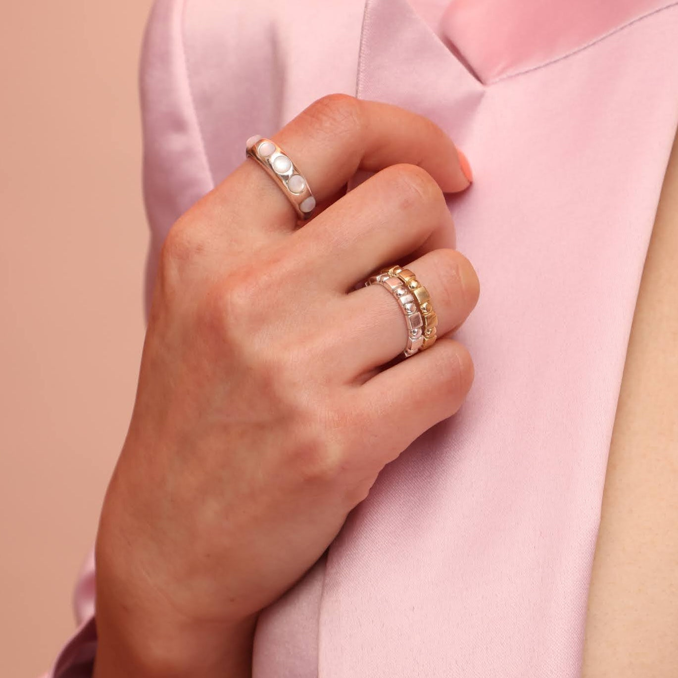 Close up of a person wearing three rings, one in silver with mother of pearl stones and two stacked shapes bands with alternating square and circle patterns.