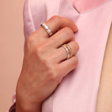 Close up of a person wearing three rings, one in silver with mother of pearl stones and two stacked shapes bands with alternating square and circle patterns.