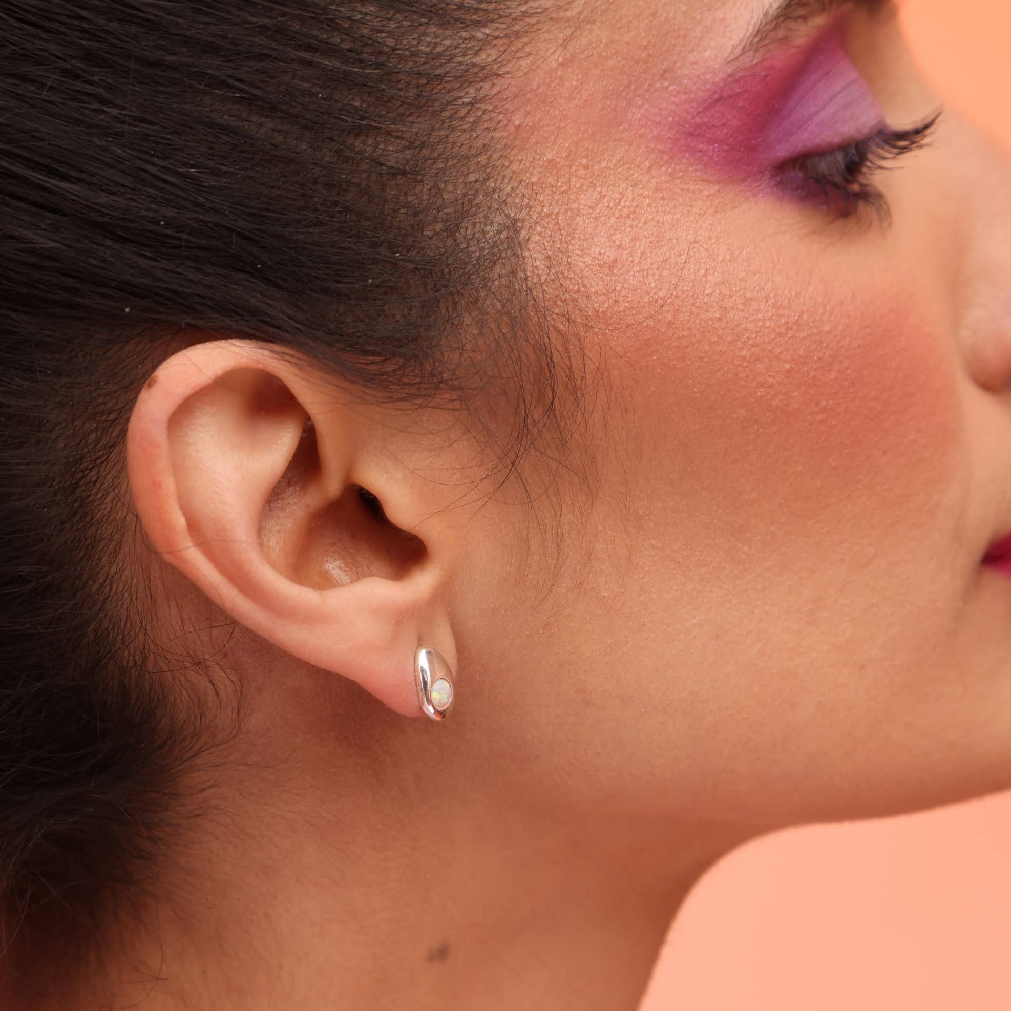 A side profile of a person wearing a teardrop-shaped earring in silver with an opal stone