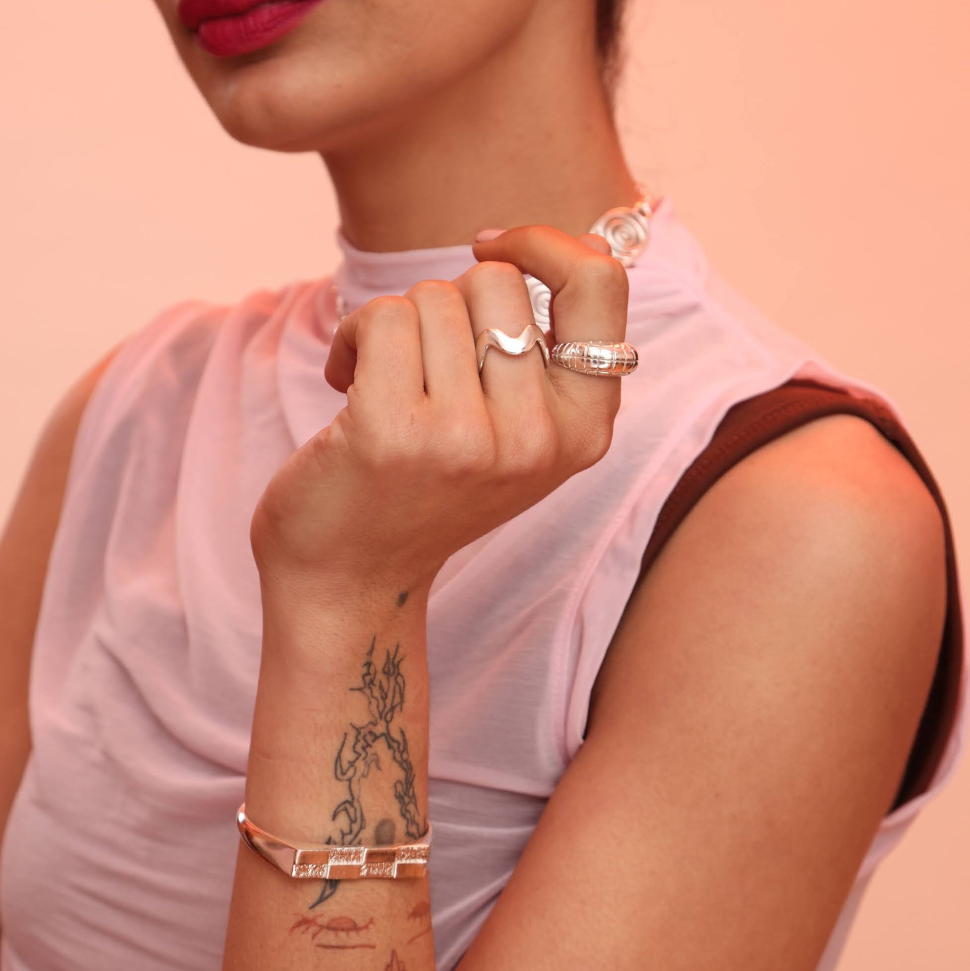 Person wearing a silver wavy ring and a bubble ring with a grid pattern on it as well as a silver bracelet with a checkerboard pattern