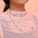 Person wearing layered silver necklaces, one with silver spiral charms and one paperclip chain with a spiral clasp