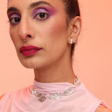 A person wearing a pink top and a silver-colored geometric necklace that resembles a spiral pattern