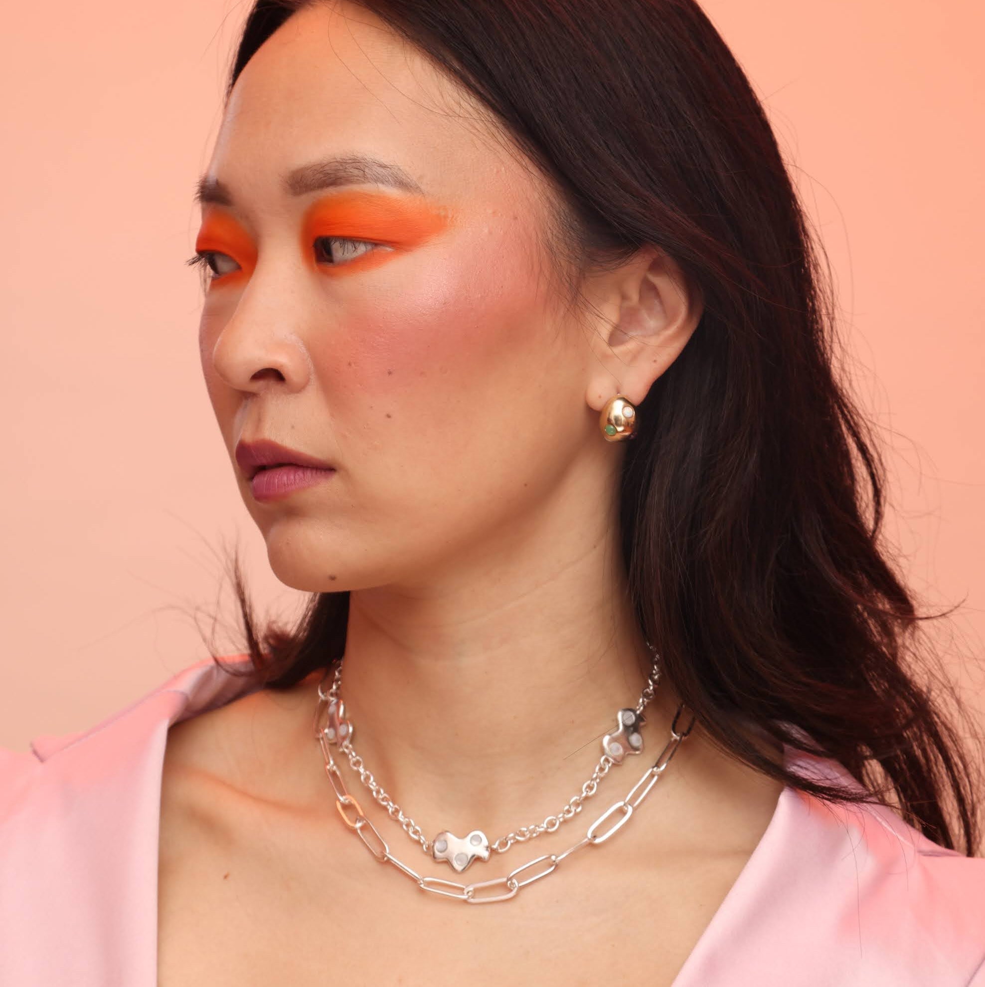 A person wearing a silver necklace with three cloud charms with mother of pearl cabochon stones layered with a paperclip chain necklace