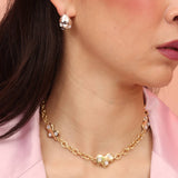 A person wearing a gold-colored necklace with three charms shaped like artist palettes and mother of pearl stones