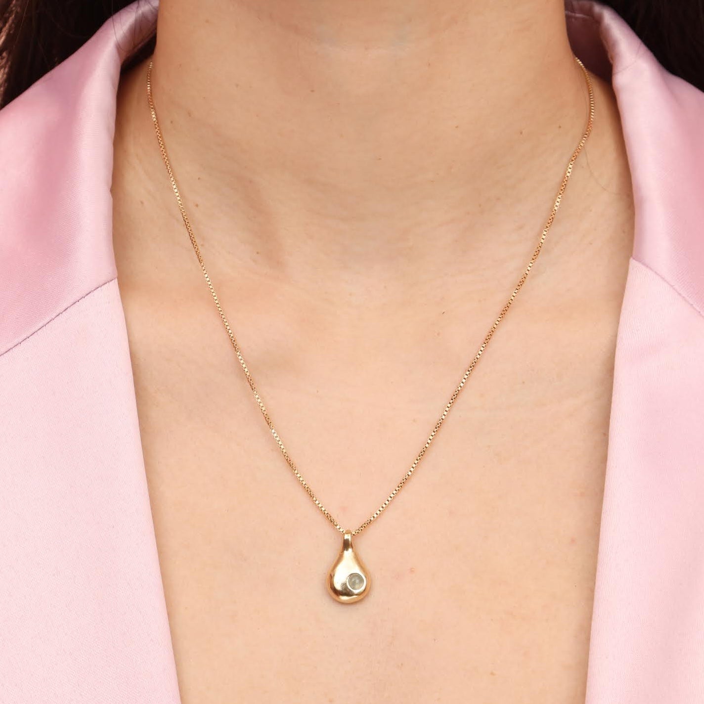 A person wearing a gold colored bronze teardrop necklace with a blue aquamarine stone