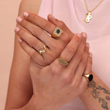 Person wearing a variety of gold colored rings including a square signet with a green inlay stone