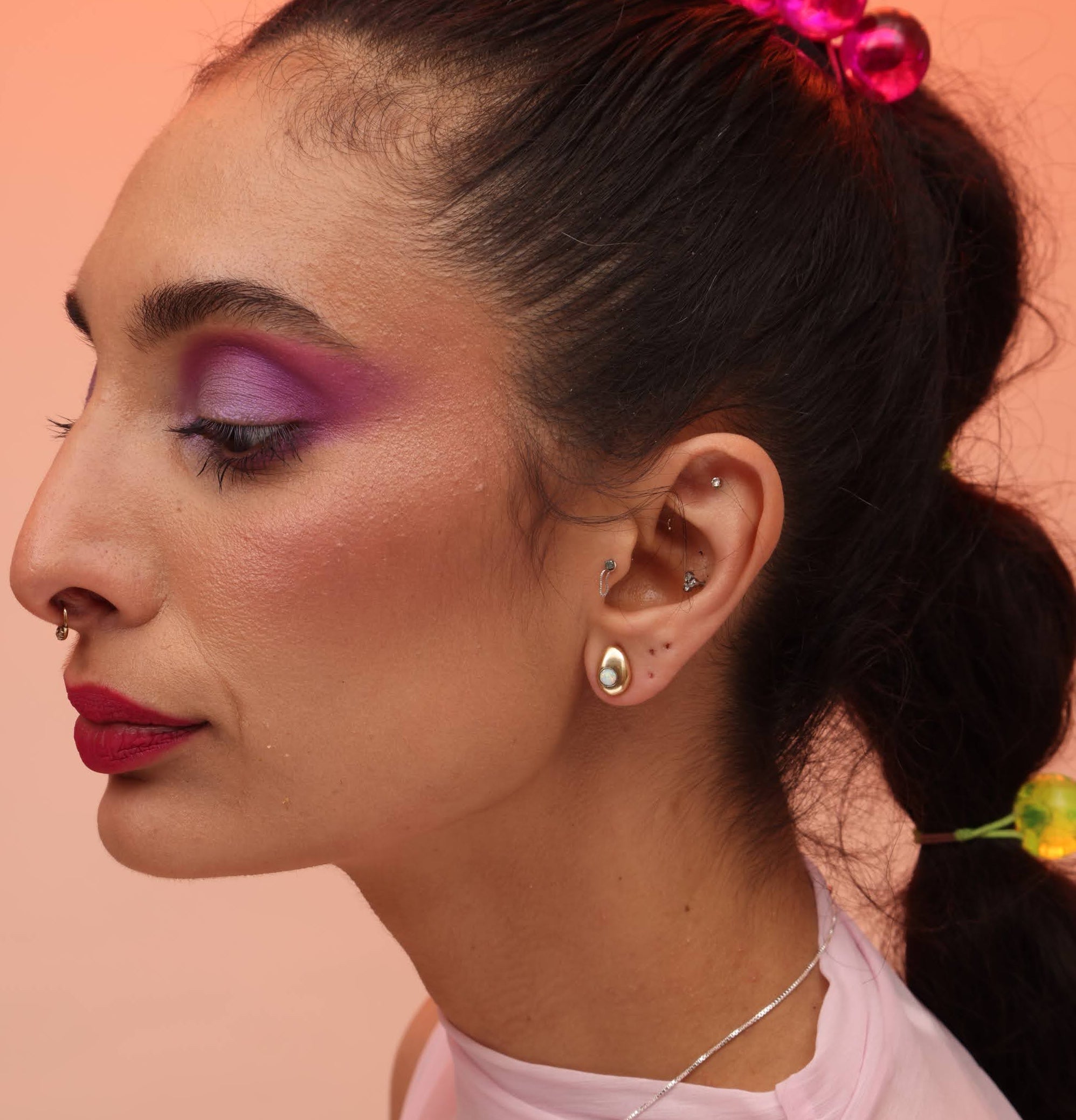 A person wearing a bronze teardrop post earring with an opal stone