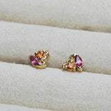 Pair of gold earrings with pink and orange gemstones on a cream cushion