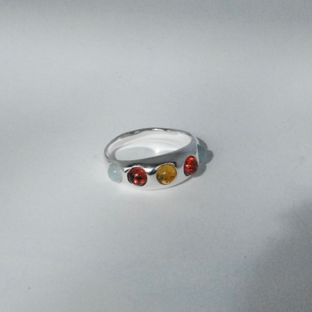 A silver ring with red, yellow and blue cabochon inlay stones displayed on a grey background