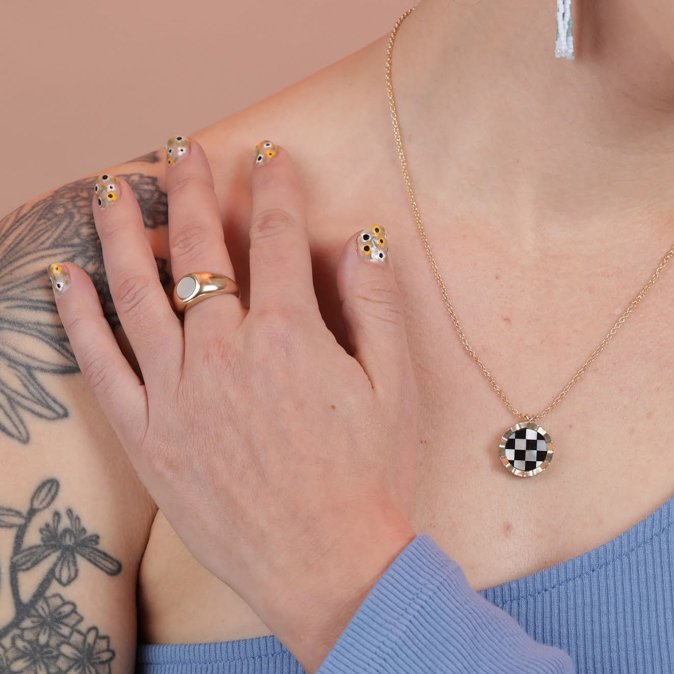 A person wearing a gold toned necklace with a wavy border around a checkerboard inlay pattern