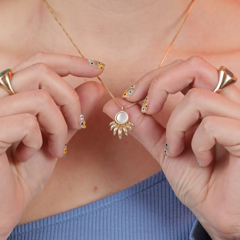 Person wearing and holding a bronze gold toned necklace with a ray shaped pendant and mother of pearl inlay stone