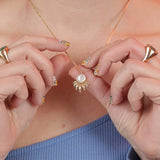 Person wearing and holding a bronze gold toned necklace with a ray shaped pendant and mother of pearl inlay stone