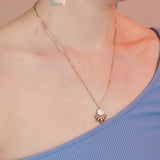 Person wearing a bronze necklace with a delicate box chain and a ray shaped pendant with white mother of pearl stone