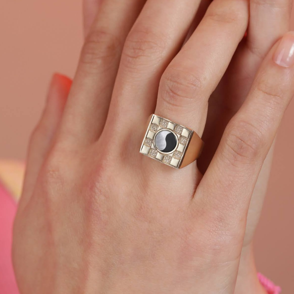 A person wearing a square checkerboard inlay ring with a visible black and white ying yang inlay design on their finger.