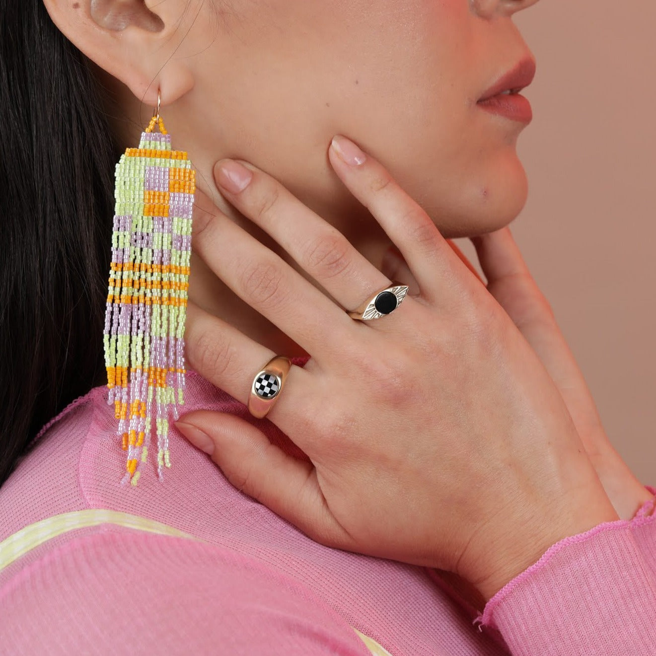 A person wearing beaded earrings and two rings, one eye shaped with a black onyx center