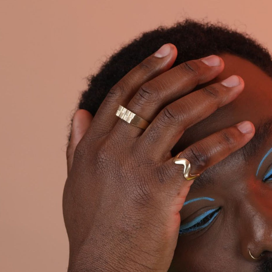 Person wearing two gold toned bronze rings, one wavy pattern and one checkerboard signet