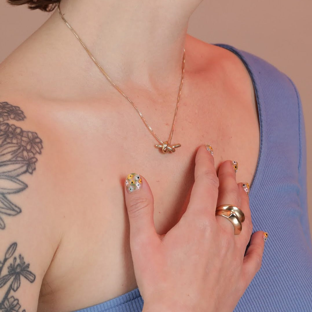 Photo of a person's chest with a hand, wearing a knot necklace in bronze and two stacked rings in bronze