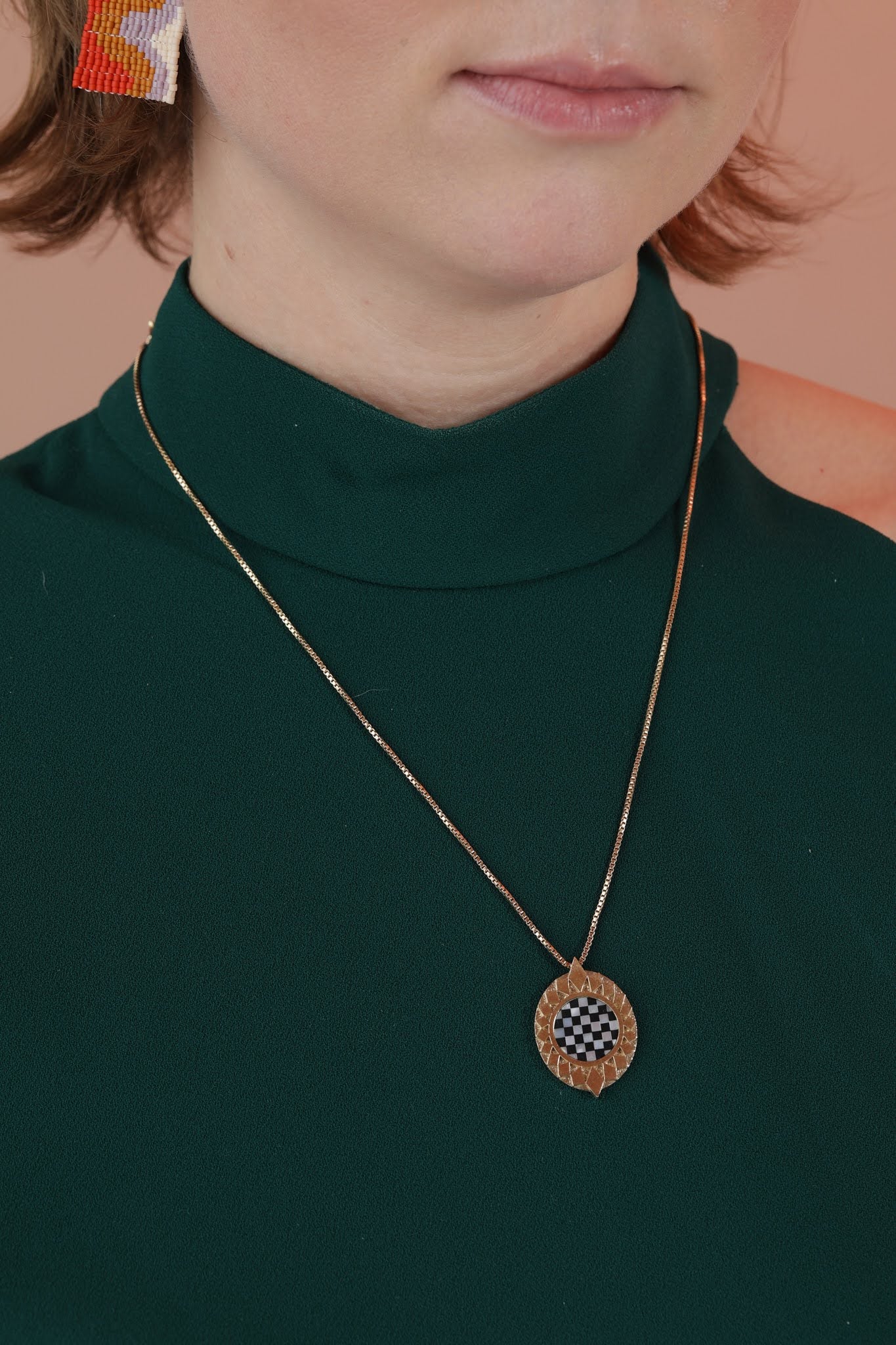 Person wearing a bronze pendant with a starburst design surrounding a checkerboard black and white inlay stone