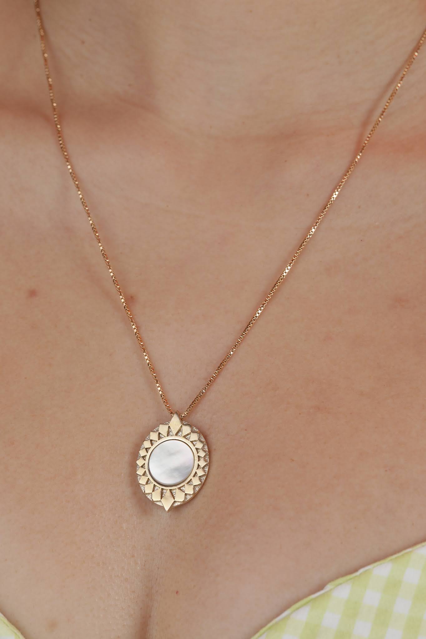 Person wearing a bronze pendant with a starburst design surrounding a white mother of pearl inlay stone