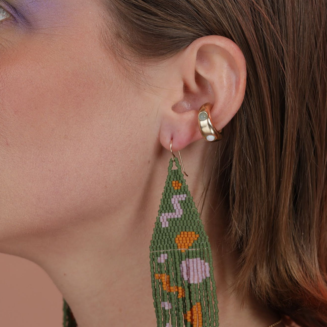 A woman wearing a beaded earring and a gold colored ear cuff with stones