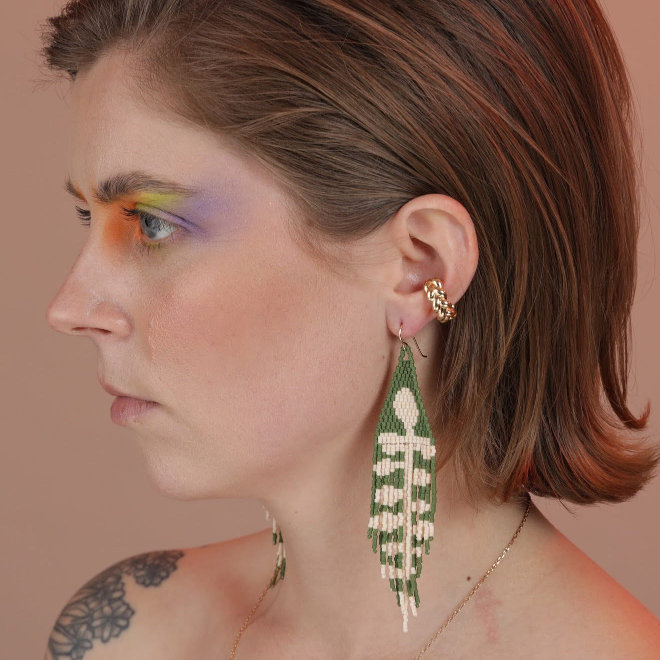 Person wearing a gold braided ear cuff with green and cream beaded earrings