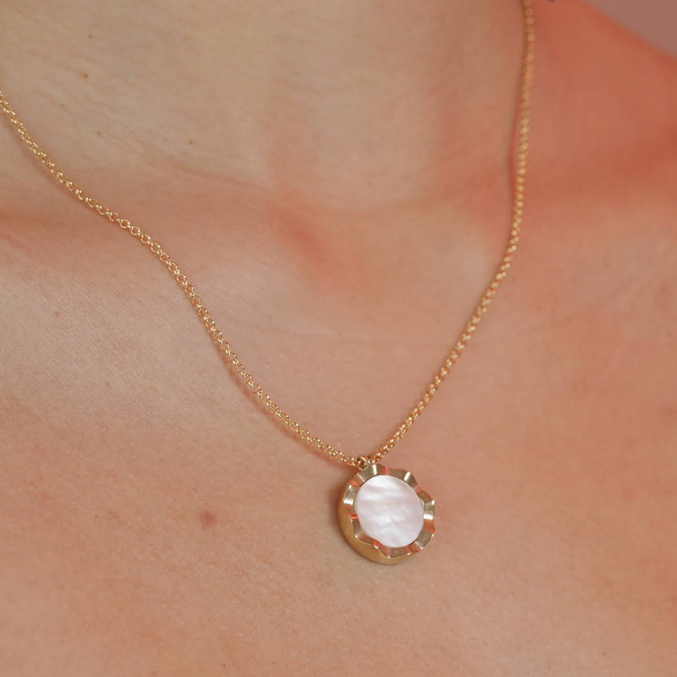 A woman wearing a gold colored pendant with a squiggly border and mother of pearl inlay