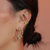 Woman wearing a gold knot earring and a ridged gold ear cuff