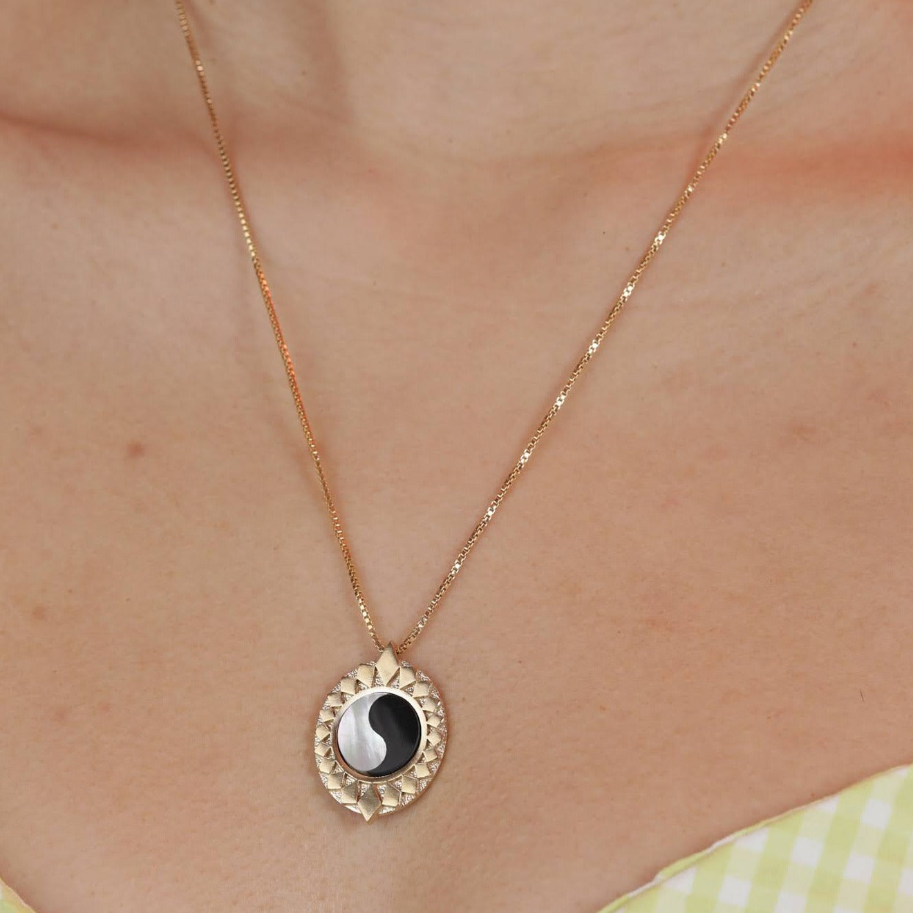 Person wearing a bronze pendant with a starburst design surrounding a ying yang inlay stone