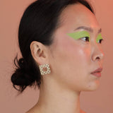 Person wearing gold colored bronze square earrings with a checkerboard pattern