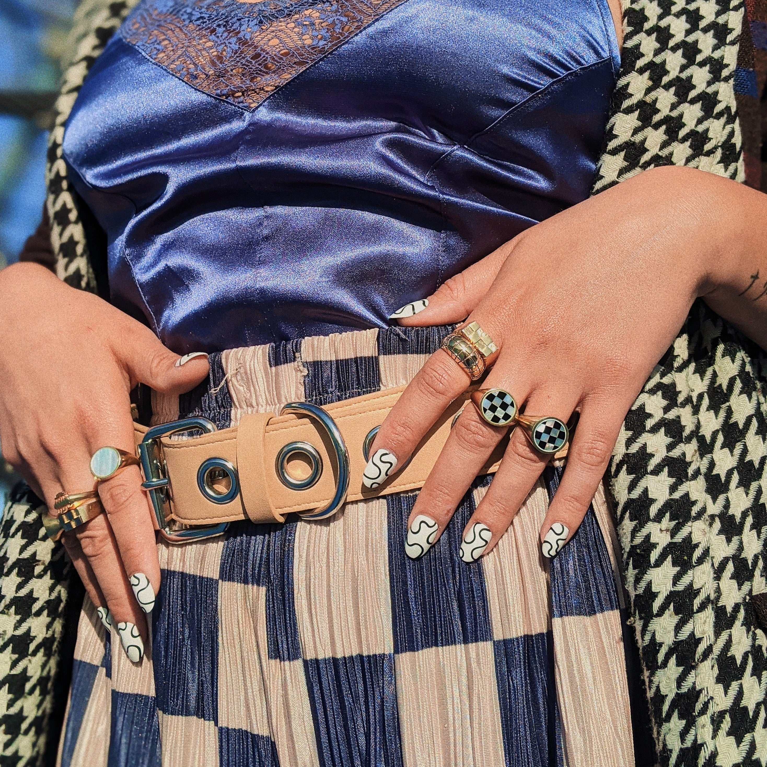 Person wearing a patterned outfit with many signet rings on including gold and checkerboard ones