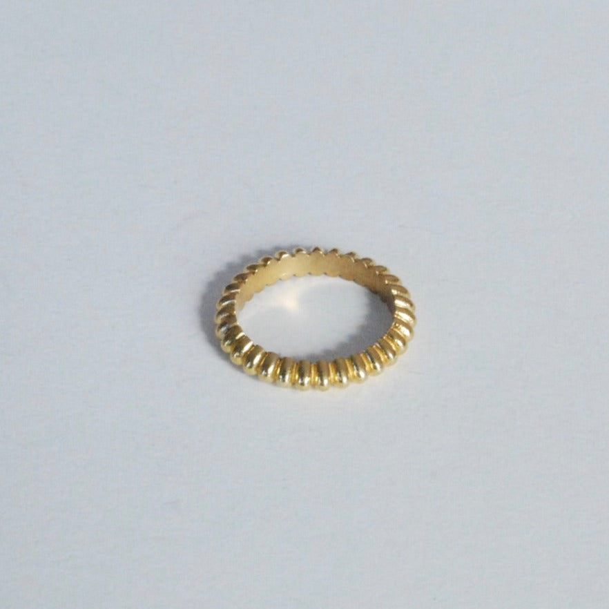 A gold-colored band ring with a geometric design, displayed on a white background.