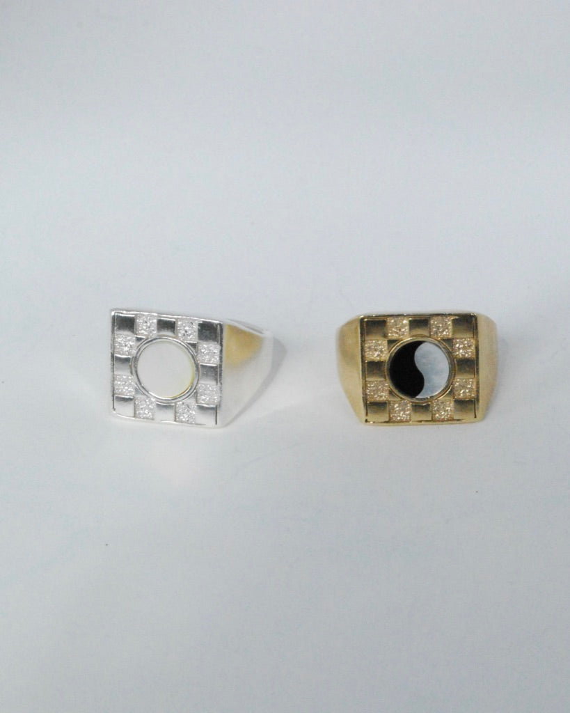 Two square checkerboard rings, one in silver with a white mother of pearl stone and one in bronze with a black and white ying yang pattern
