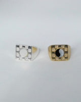 Two square checkerboard rings, one in silver with a white mother of pearl stone and one in bronze with a black and white ying yang pattern