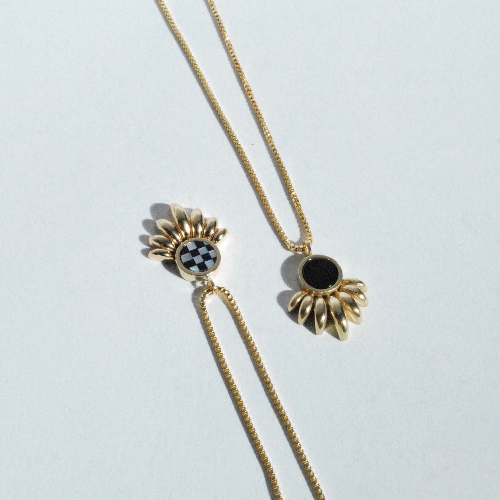 Two bronze colored ray shaped necklaces with checkerboard inlay and black onyx inlay on a white background