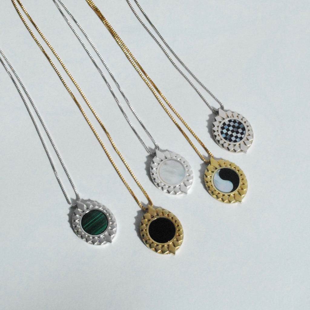 Silver and bronze pendants with sunburst style patterns surrounding stone inlay in green, black, white, checkerboard and ying yang inlay