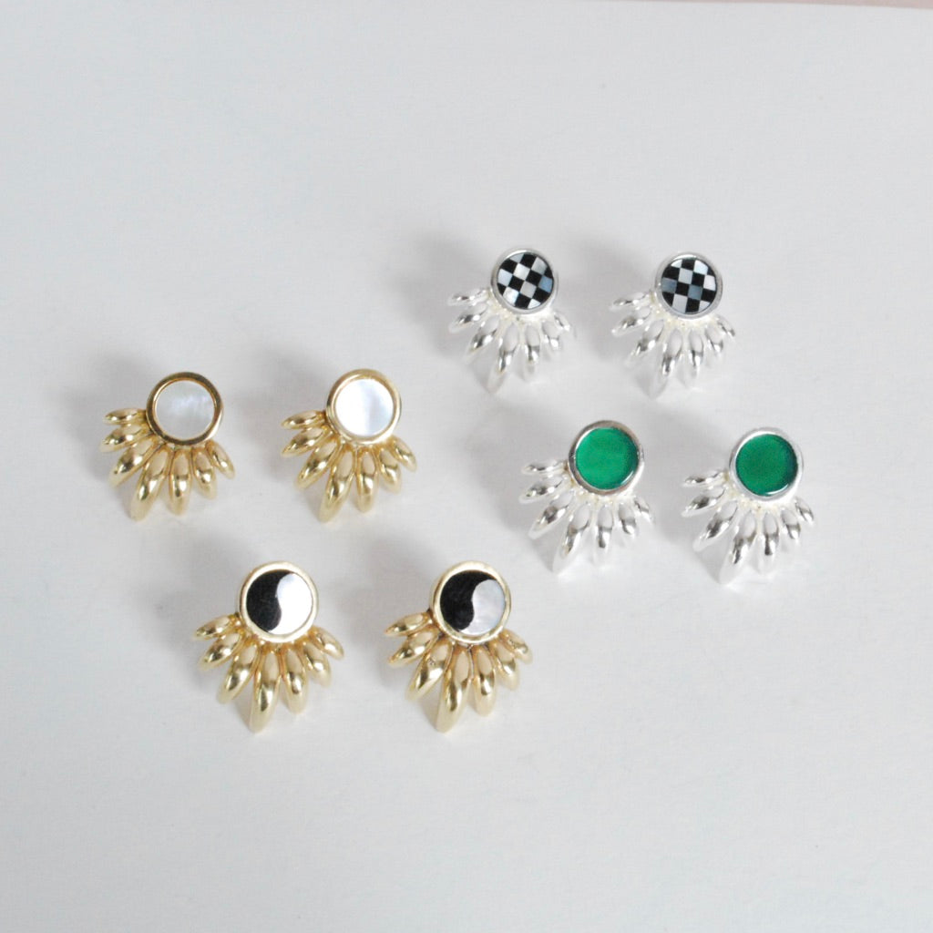 A collection of inlay earrings displayed on a surface, featuring various designs with inlayed stones in bronze or silver sunray patterns.