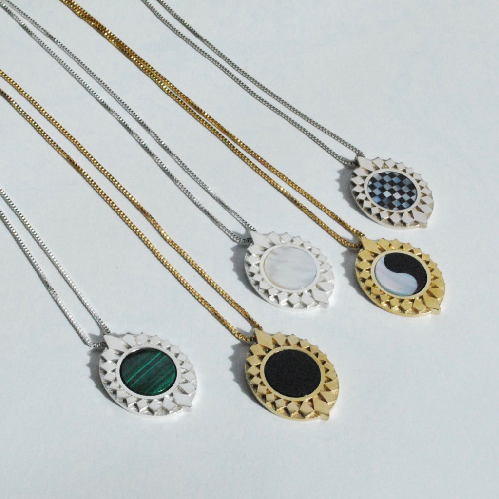 A collection of diamond burst pendants with various inlay stones, displayed on a white surface.