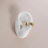A gold-colored ear cuff resting on a white ear mold, showcasing its curved design.