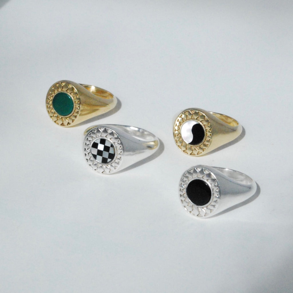A collection of four rings with inlay stones, two with gold settings and two with silver settings, each surrounded by a decorative star border.