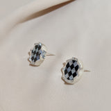 Photo of silver earrings from the side with a squiggly border and checkerboard black and white inlay stone