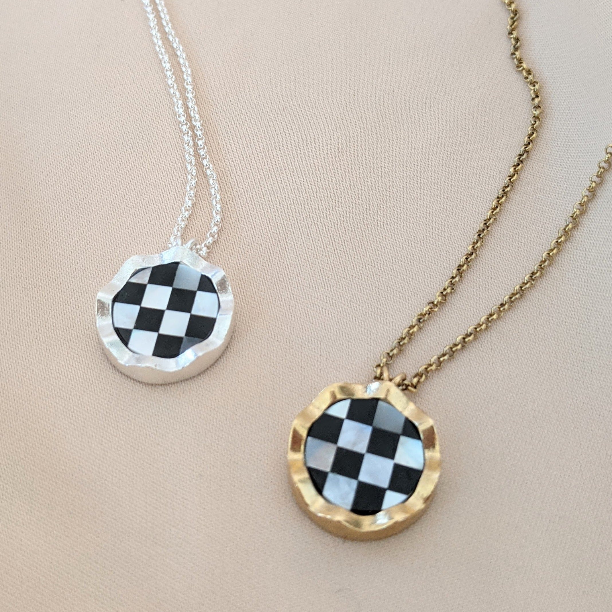 Two necklaces with checkerboard stones and wavy borders in silver and bronze lying on a cream background