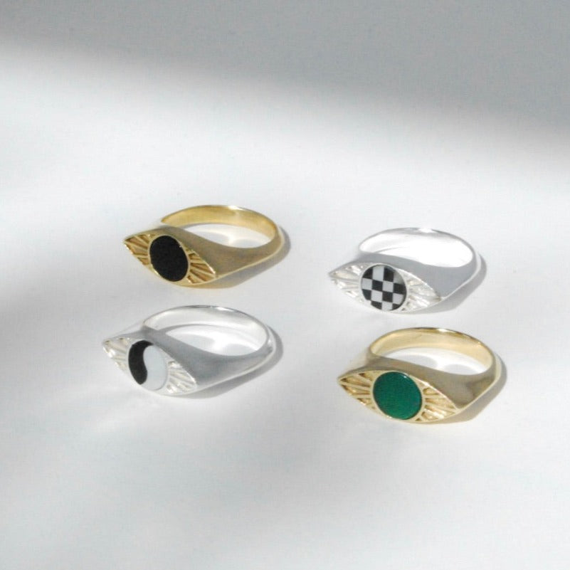 A collection of four eye shaped rings with inlay designs in black, green, checkerboard and ying yang displayed against a light background.