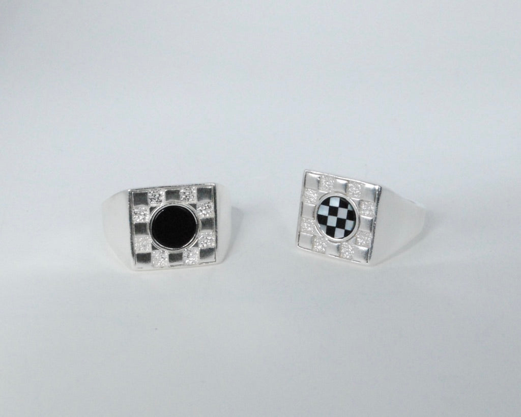 Two square checkerboard rings on a grey background, one with black onyx inlay and one with black and white checkerboard inlay