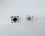 Two square checkerboard rings on a grey background, one with black onyx inlay and one with black and white checkerboard inlay