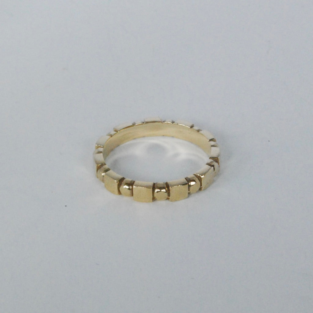Ring with alternating cube and sphere patterns in a gold bronze color on a grey background