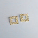 A pair of gold-colored square checkerboard earrings on a light background.