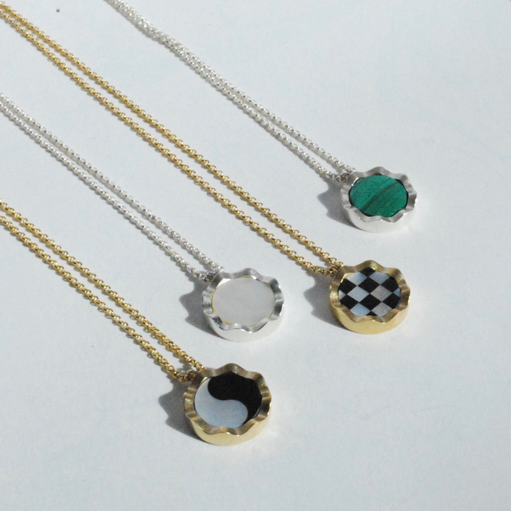 A collection of squiggly inlay necklaces with different stone options and gold and silver borders displayed on a white surface.