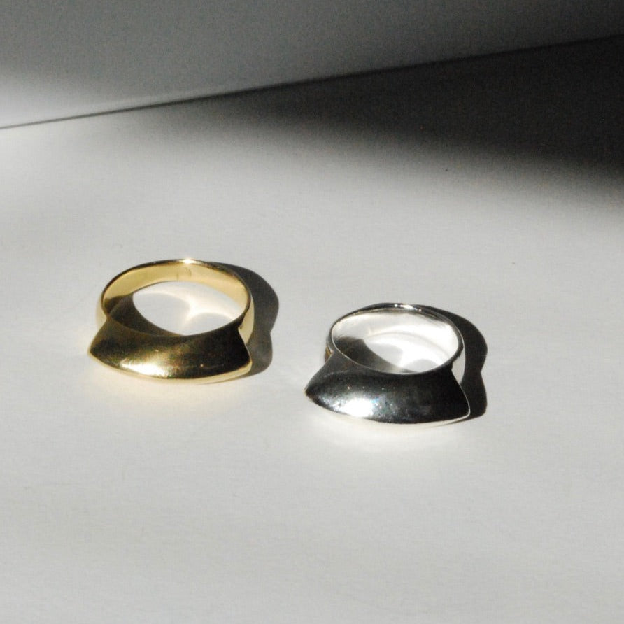Two fan shaped rings, one gold-colored and one silver-colored, placed side by side on a light surface.