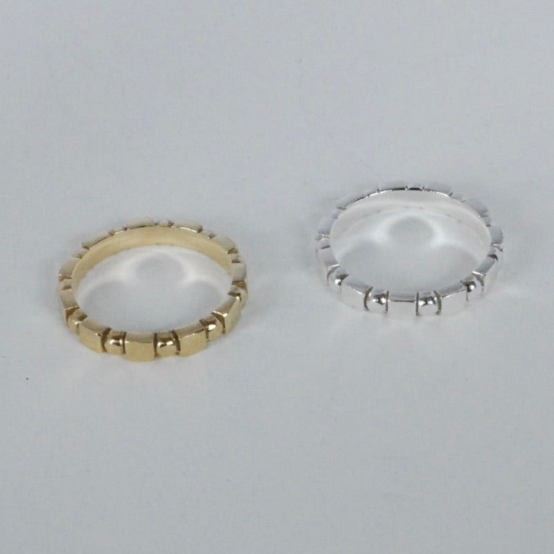 Two rings, one in gold color and the other in silver, with a simple geometric shape design placed side by side on a white surface.