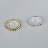 Two rings, one in gold color and the other in silver, with a simple geometric shape design placed side by side on a white surface.